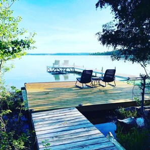 Une jetée en bois avec deux chaises longues donnant sur un lac paisible, le tout entouré de verdure.