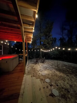 A wooden deck with string lights, a hot tub, and a stone pathway leading to outdoor seating.