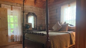 Una cama con dosel de madera con colcha, un espejo encima y una ventana con cortinas.