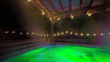 Un jacuzzi con iluminación verde, rodeado por una estructura de madera con luces de cuerda.