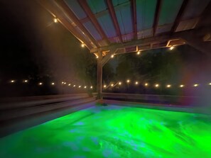 A hot tub with a green light effect, surrounded by a wooden structure with string lights.