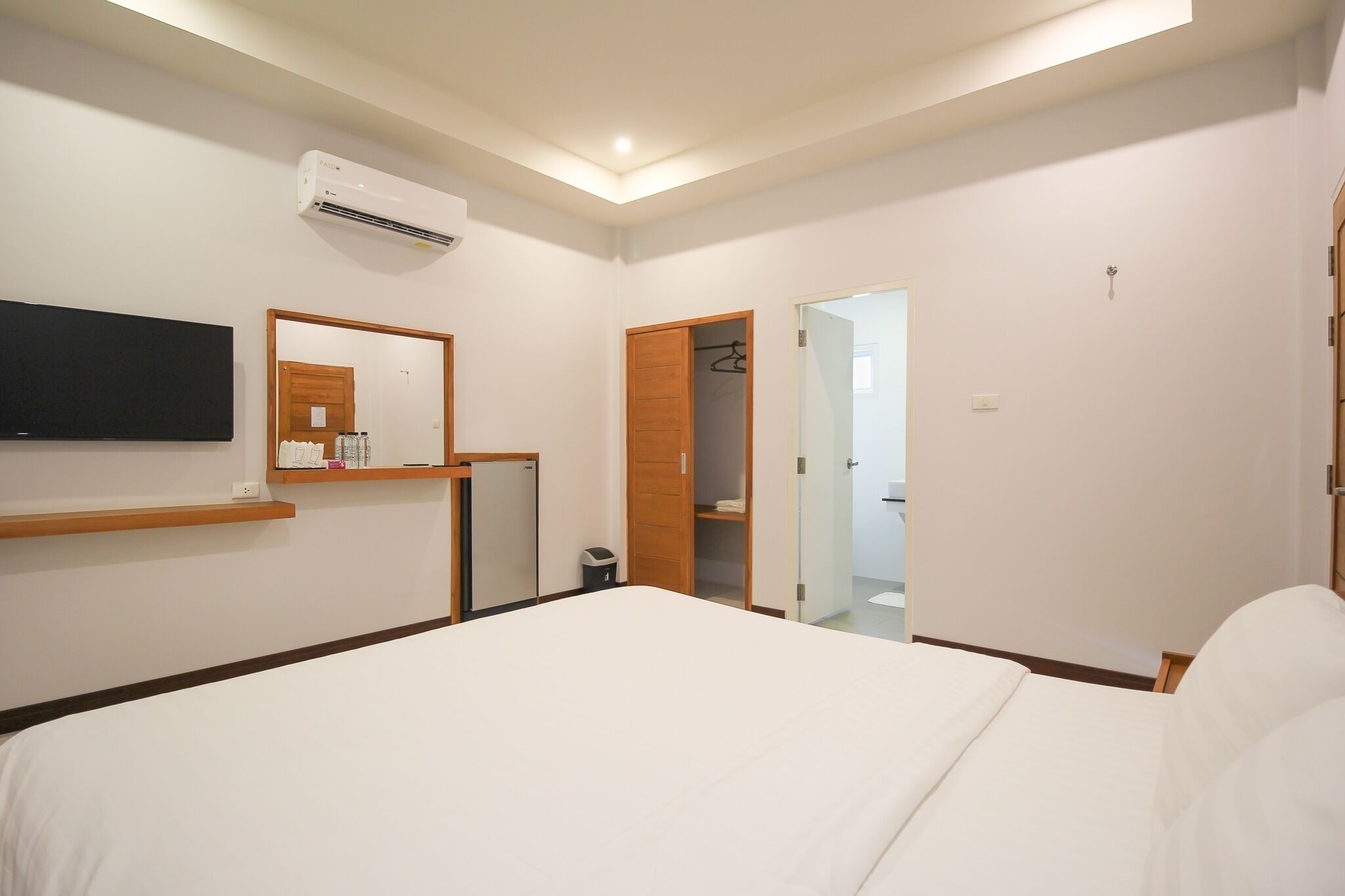 A hotel room with a bed, a mounted TV, a wardrobe, and a bathroom door.