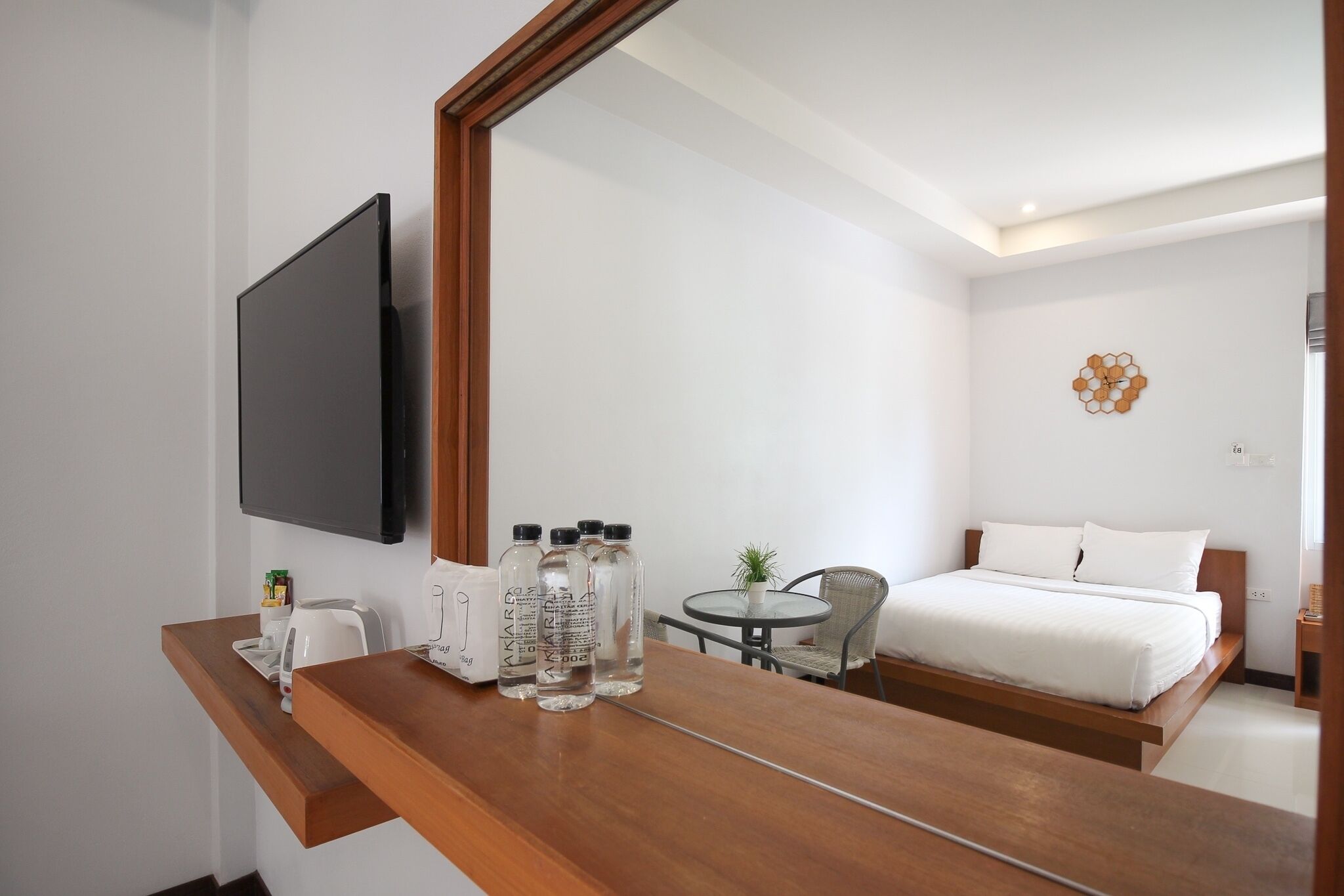 A hotel room with a wooden desk, a flat-screen TV, a bed with white bedding, a small round table with a chair, and a decorative wall piece.