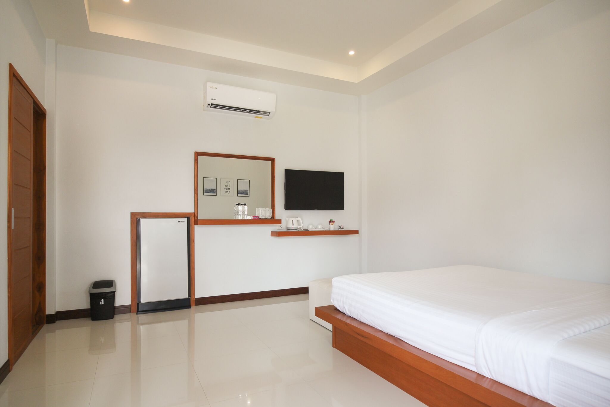 A modern hotel room with a large bed, a small desk with a mirror, a flat-screen TV, and a built-in air conditioning unit.