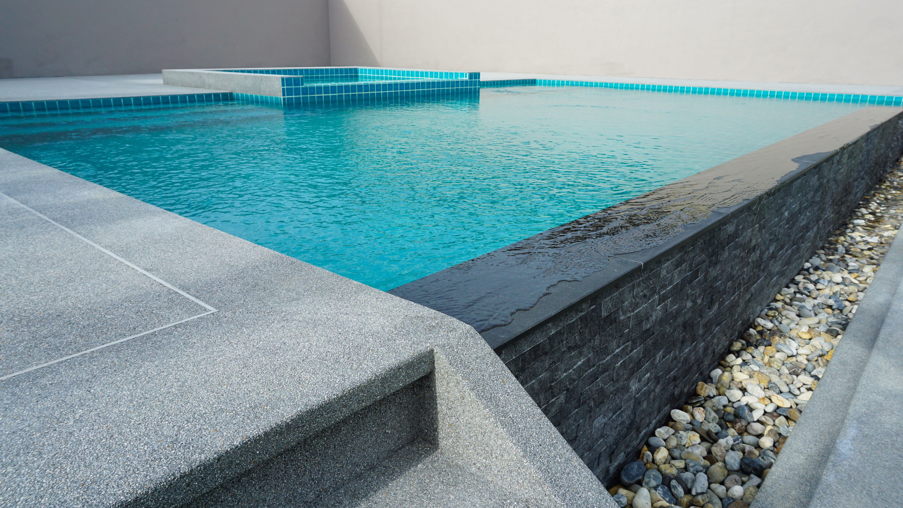 Ein Swimmingpool mit klarem, blauem Wasser, umgeben von Steinmauern und Kies.