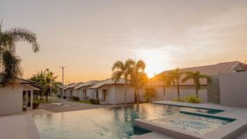 Un resort moderno con piscina, palmeras y villas con techos de tejas.