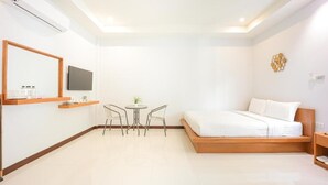Une chambre d’hôtel moderne équipée d’un lit, d’une télévision, d’une petite table avec des chaises et d’une étagère fixée au mur.