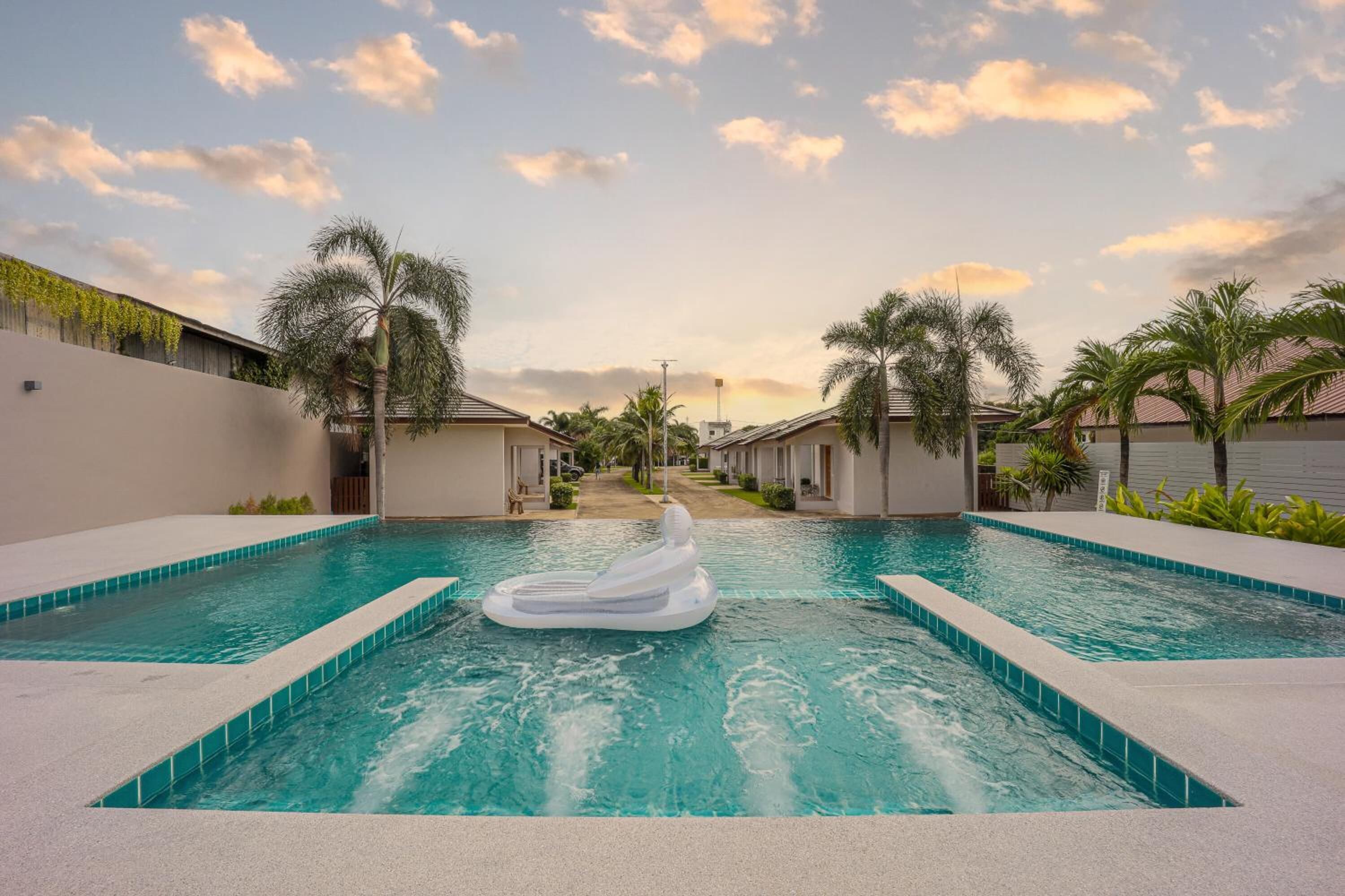 A swimming pool with a water slide, surrounded by palm trees and buildings.