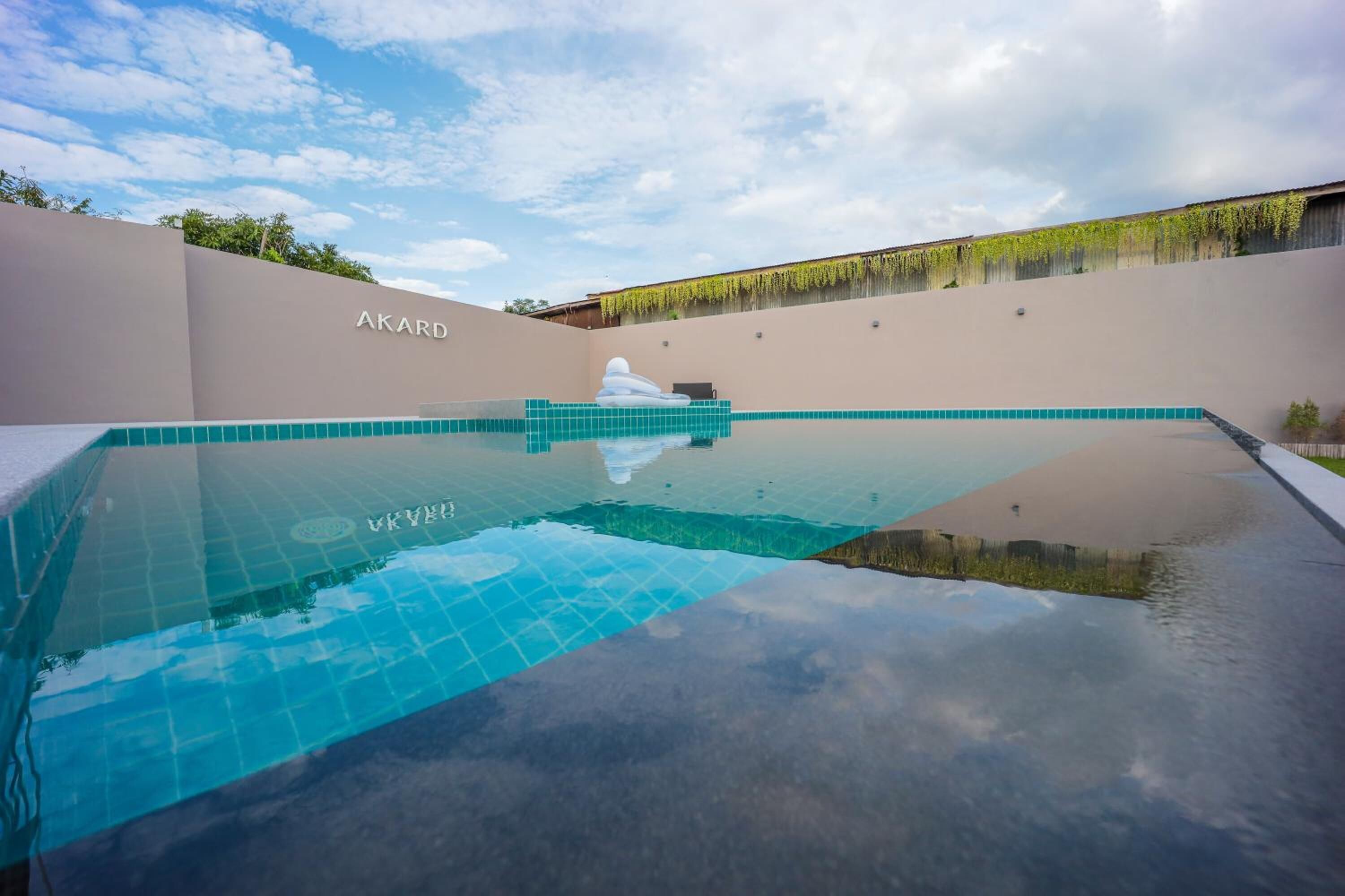 Ein Schwimmbecken mit klarer, blauer Wasseroberfläche, umgeben von einer beigen Mauer mit der Aufschrift 'AKARD'.