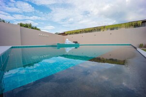 Una piscina con superficie de agua azul cristalina, rodeada por un muro beige donde se puede ver el nombre "AKARD".