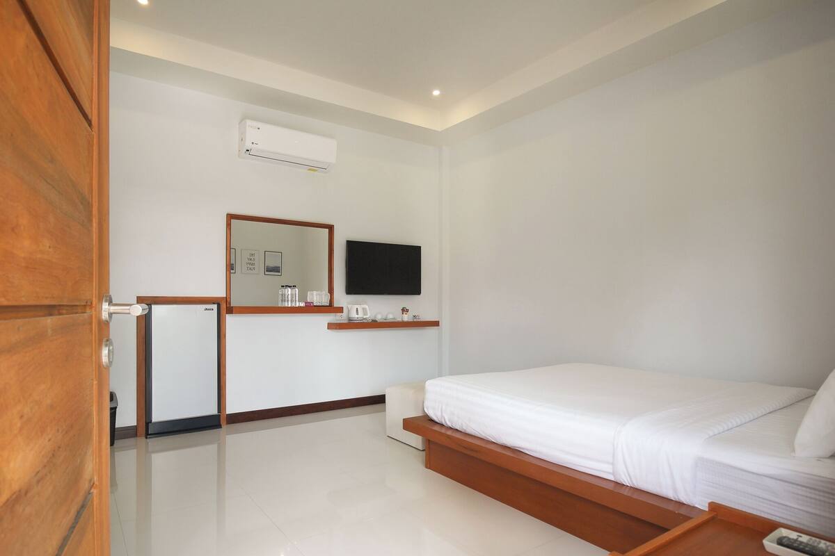 Een hotelkamer met een bed, een televisie aan de muur, een klein tafeltje met een waterkoker, en een spiegel.