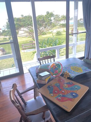 Una habitación con un ventanal grande, una mesa de madera con un rompecabezas colorido, una silla y una pequeña planta.