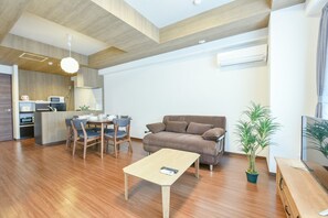 Una sala moderna con piso de madera, un sofá marrón, una mesa de comedor con sillas, una pequeña mesa de centro y una planta en maceta.