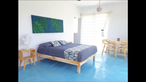 A bedroom with a bed, a small table, a chair, a wall-mounted fan, and a window with curtains. - Casa Vainilla (Isla Holbox)