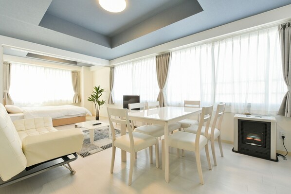 A modern hotel room with a bed, sofa, dining table, chairs, a TV, and a fireplace.