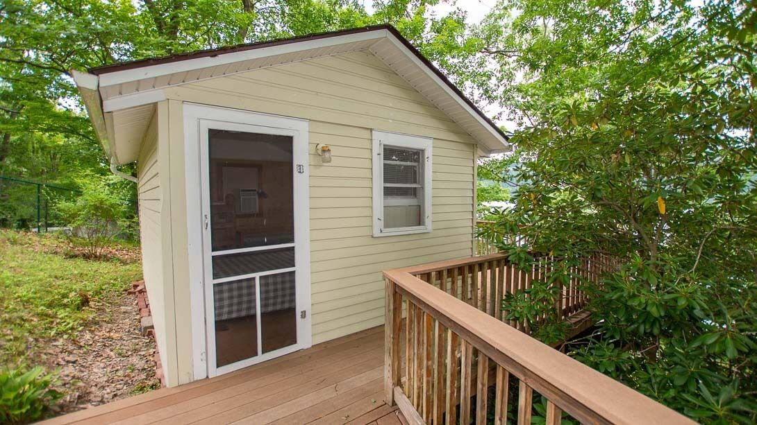 A small, single-story house with a wooden deck and a sliding glass door leading to a screened-in porch.