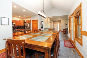 A spacious kitchen with wooden cabinets, a stainless steel refrigerator, and a dining area with a large wooden table and chairs. - Spacious 5BR Retreat with Hot Tub, Fireplace & Game Room | Galena Territory (Galena)