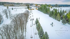 A ski resort with a ski lift, snow-covered trees, and a building in the background.