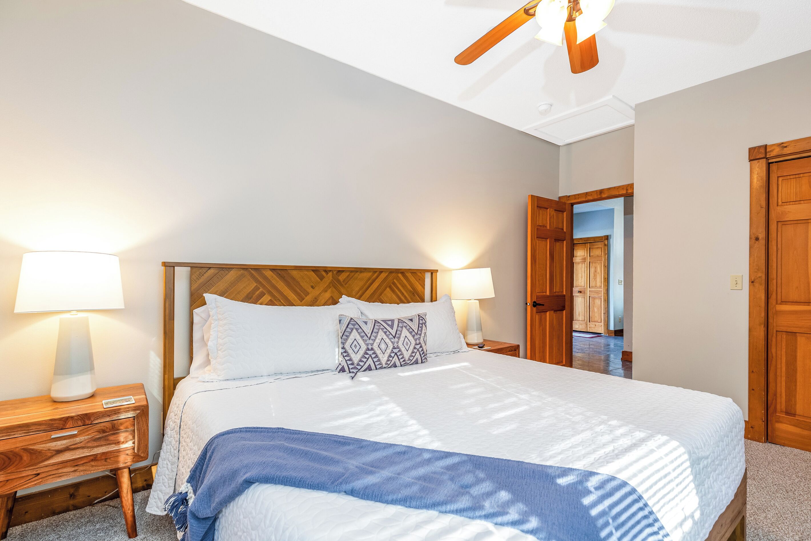 Una habitación de hotel con una cama, una mesita de noche, una lámpara, un cabecero de madera y una puerta.