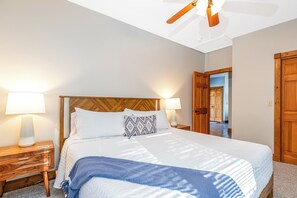Une chambre d’hôtel avec un lit, une table de chevet, une lampe, une tête de lit en bois et une porte.