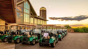 Una fila de carros de golf estacionados frente a un edificio con ventanas amplias y un silo al fondo.