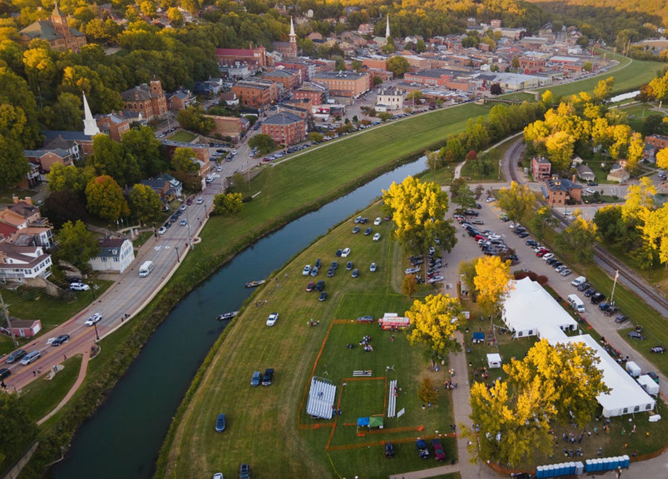 An aerial view of a town with a river, buildings, and a large open field with tents.