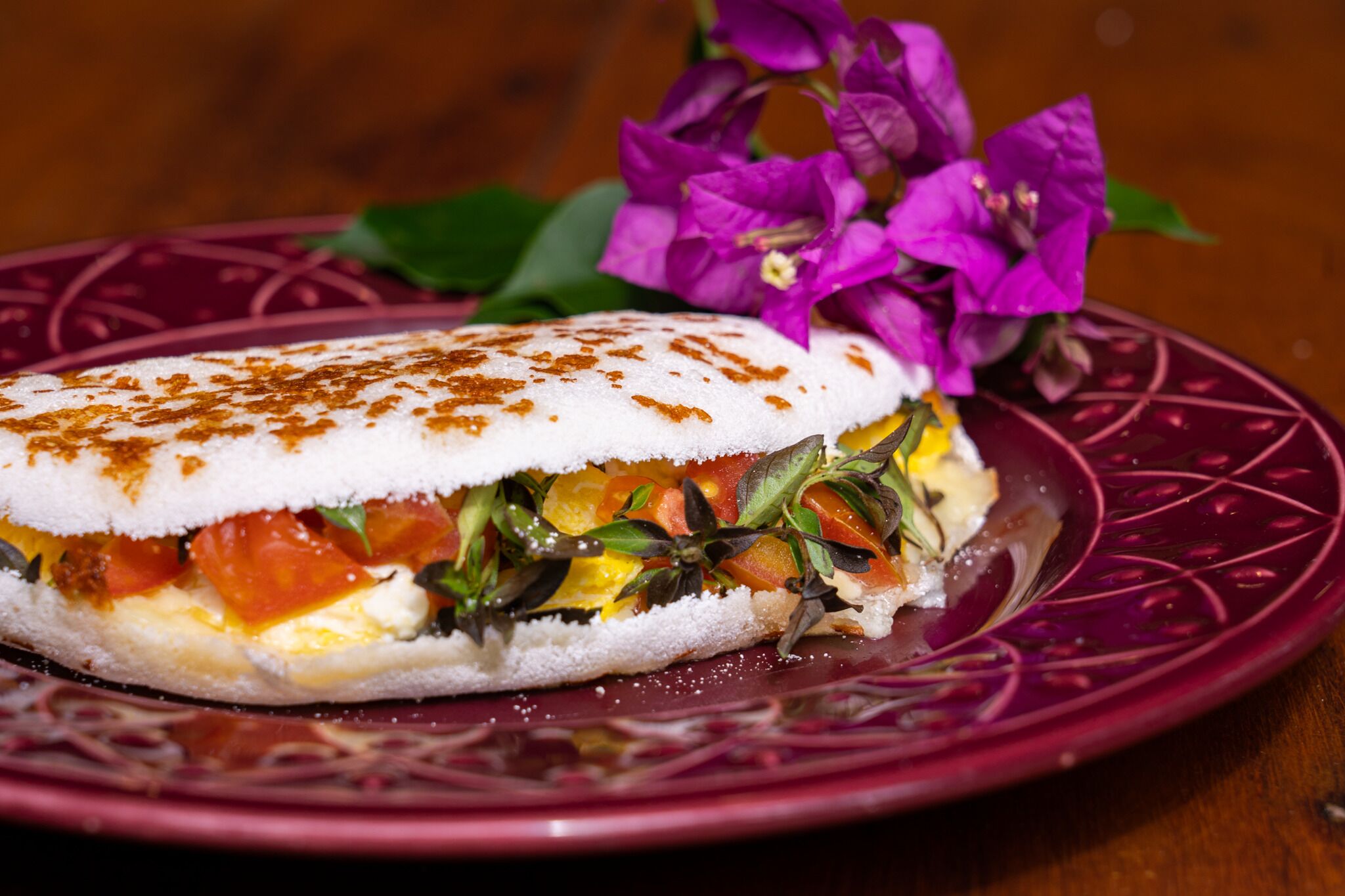 A sandwich with a white bread base, tomato, cheese, and greens, served on a purple plate with a decorative pattern.