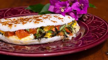A sandwich with a white bread base, tomato, cheese, and greens, served on a purple plate with a decorative pattern.