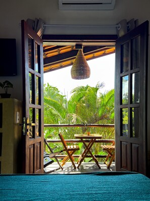 An open wooden door leading to a balcony with a hanging light fixture, a small table, and chairs. - Pousada Beira Mar (Porto Seguro)