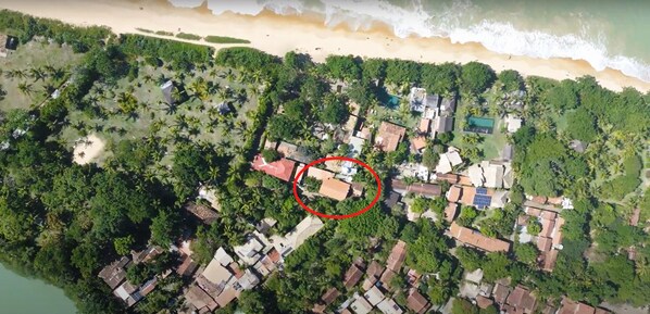 An aerial view of a coastal area with dense vegetation, a beach, and a circled building with a red roof. - Pousada Beira Mar (Porto Seguro)