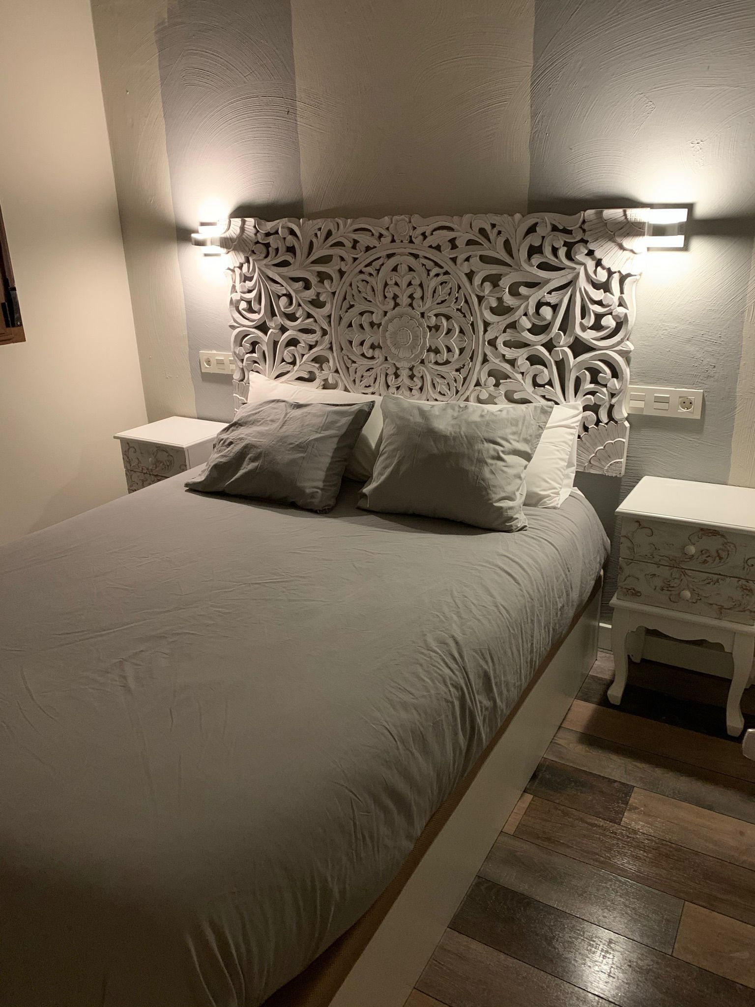 A neatly made bed with a decorative headboard, two bedside tables, and a nightstand with a lamp.