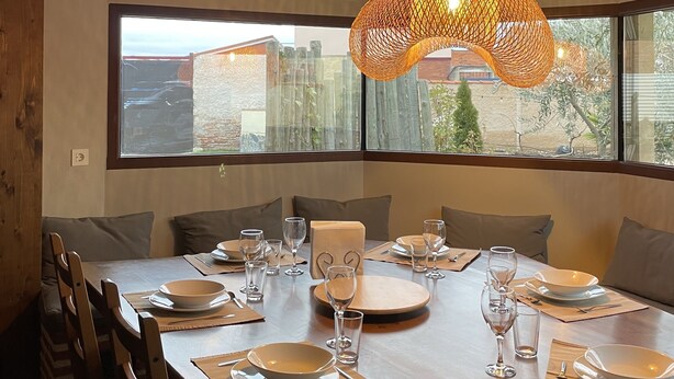 A dining area with a long wooden table set for six, large windows, and a woven light fixture. - Rural house Las Gavias  (Matapozuelos)