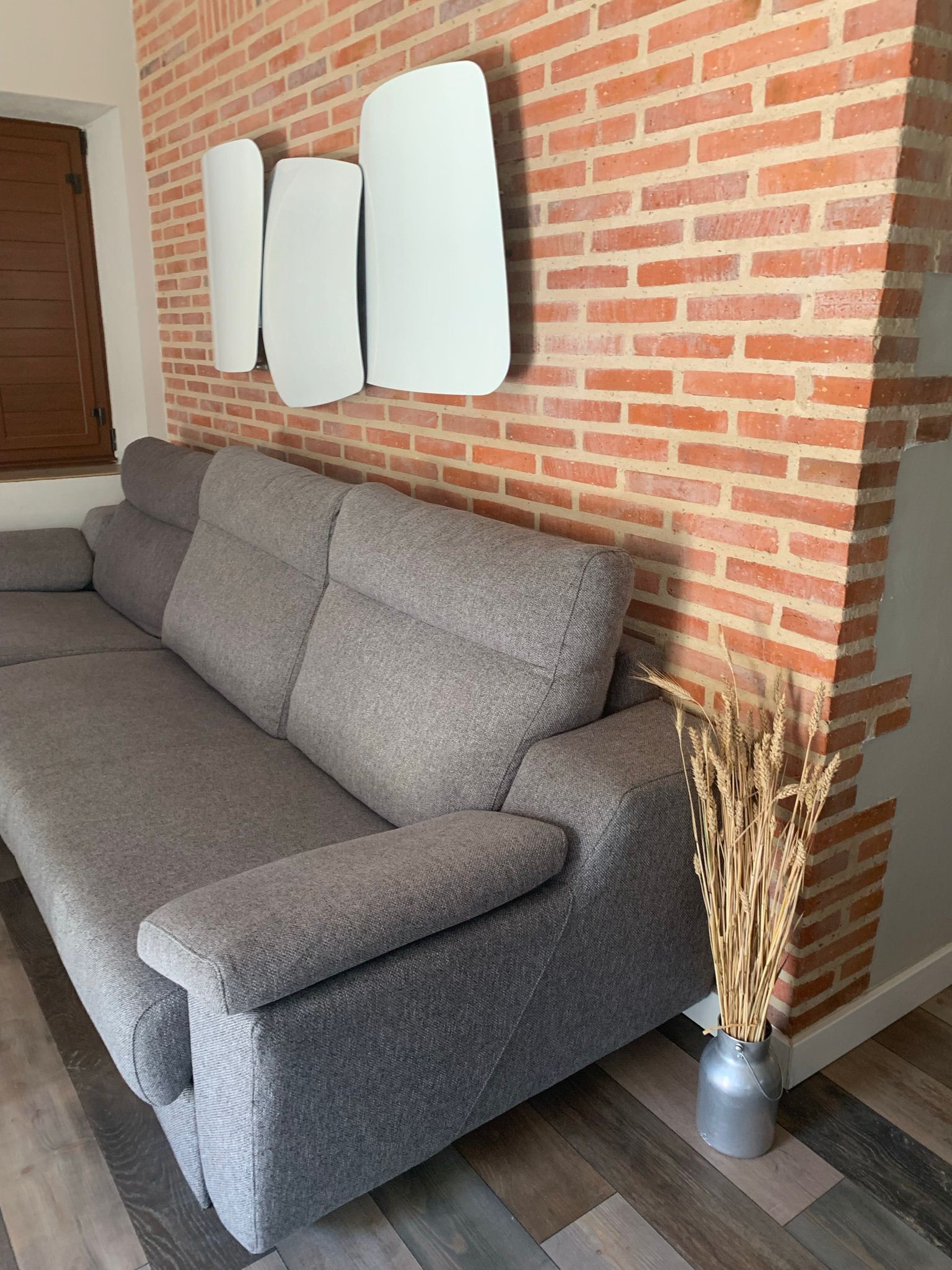 A grey sofa against a brick wall with a modern light fixture above it.