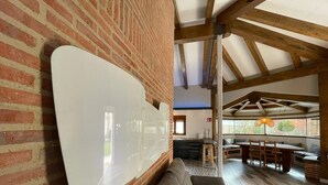 A spacious living area with a large white wall-mounted TV, a grey sofa, wooden dining table, and a kitchen in the background. - Rural house Las Gavias  (Matapozuelos)