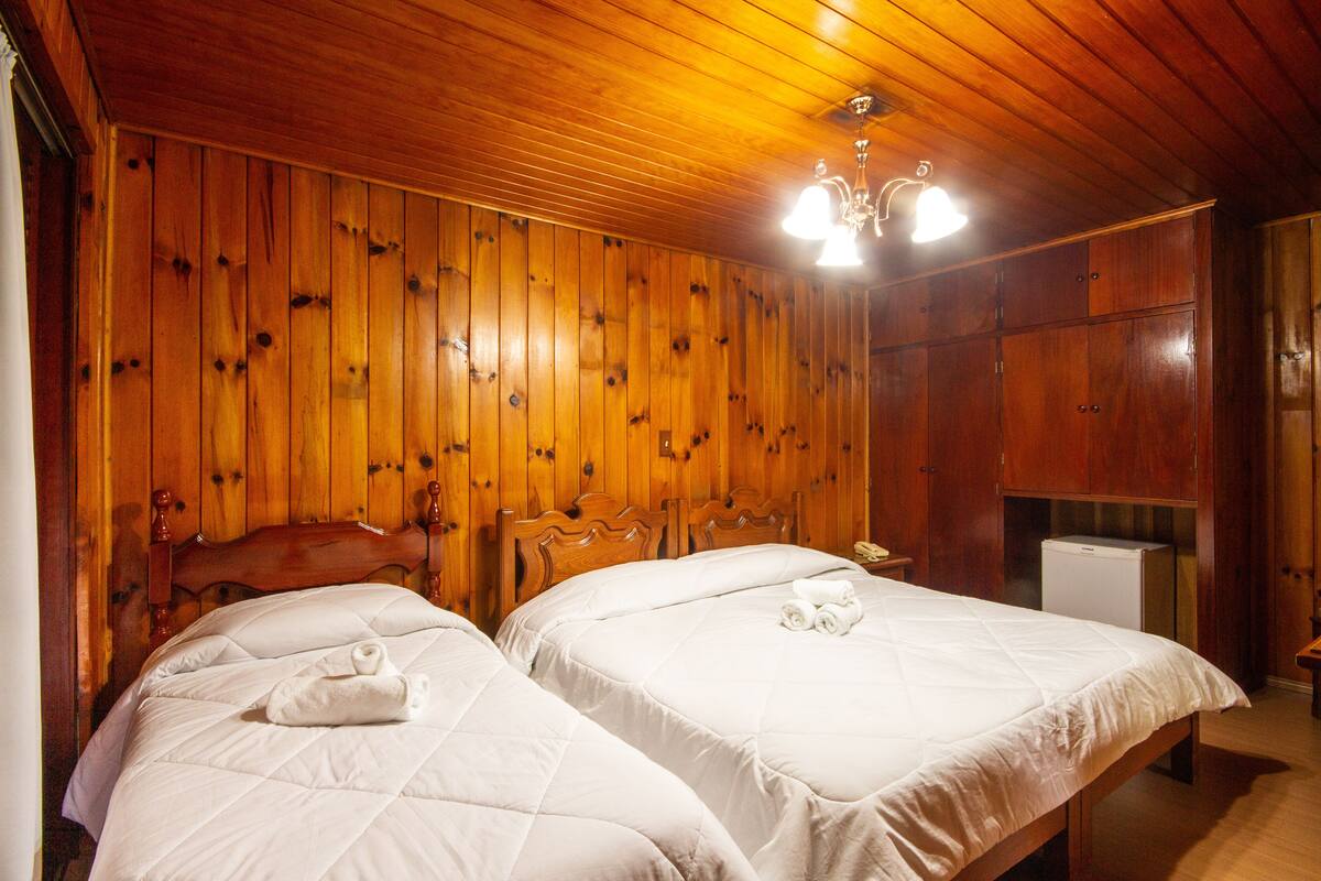 A wooden-paneled room with two beds, a wooden headboard, and a small refrigerator.