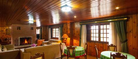 Una stanza accogliente con camino, soffitto in legno e zona pranzo con tovaglia verde.