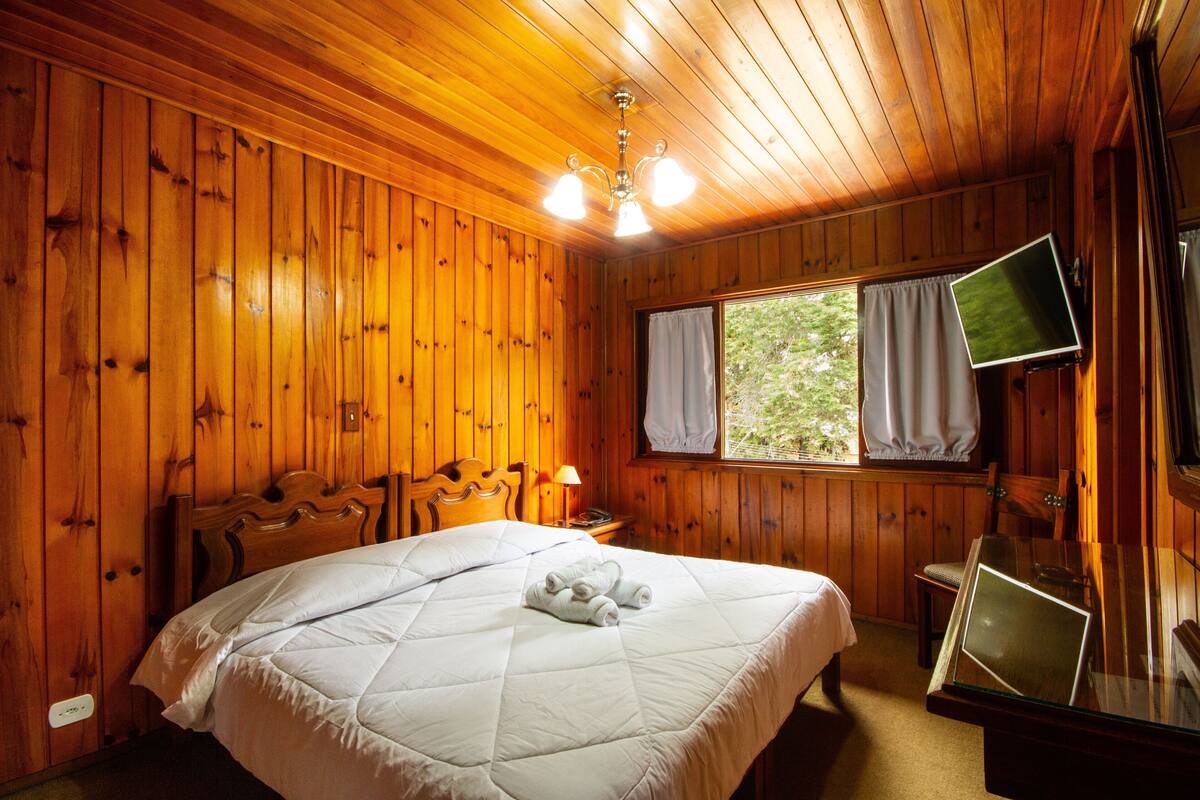 A wooden-paneled room with a bed, a television mounted on the wall, and a window with curtains.