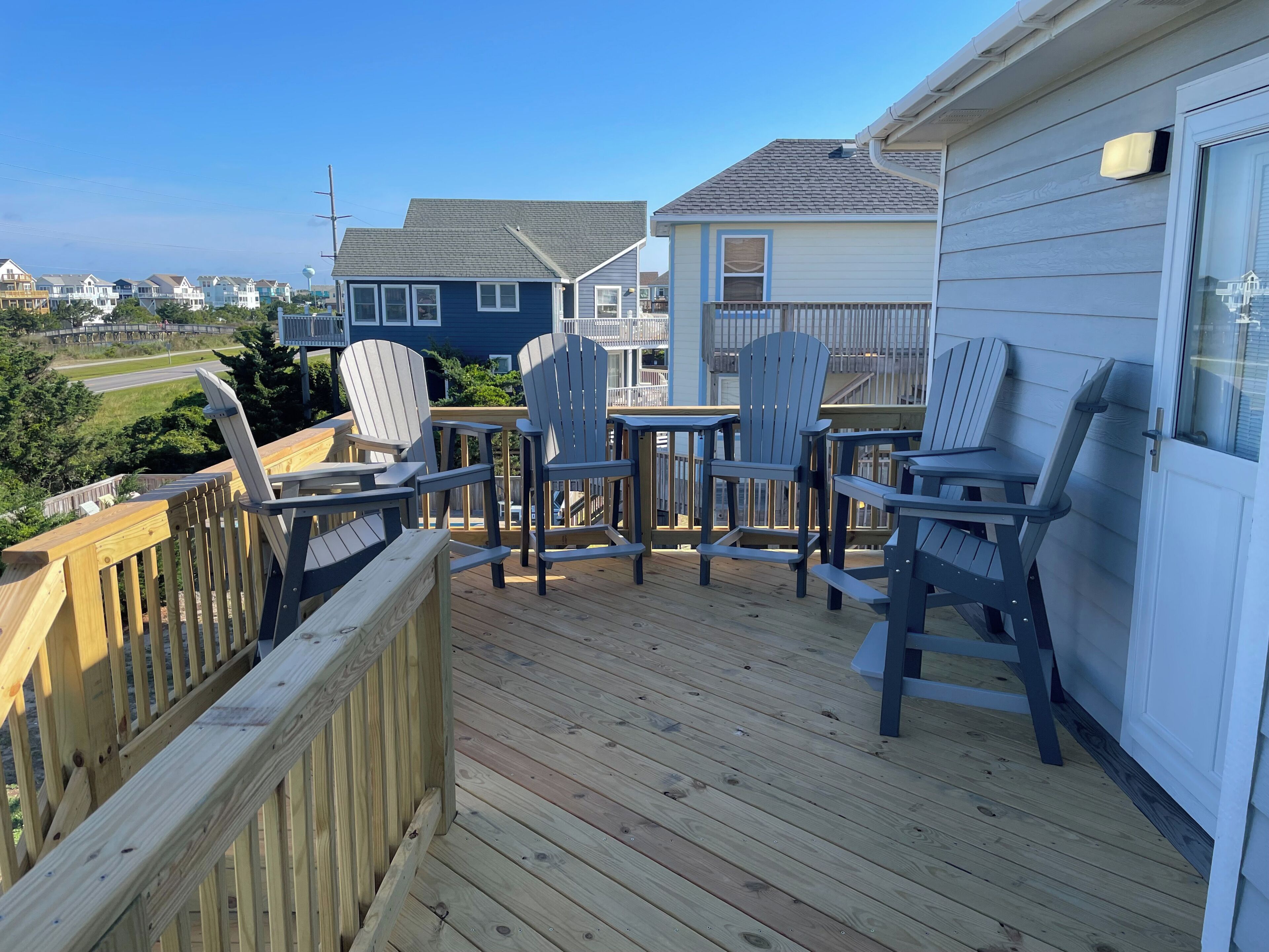 A deck with Adirondack chairs, a small table, and a view of neighboring houses.