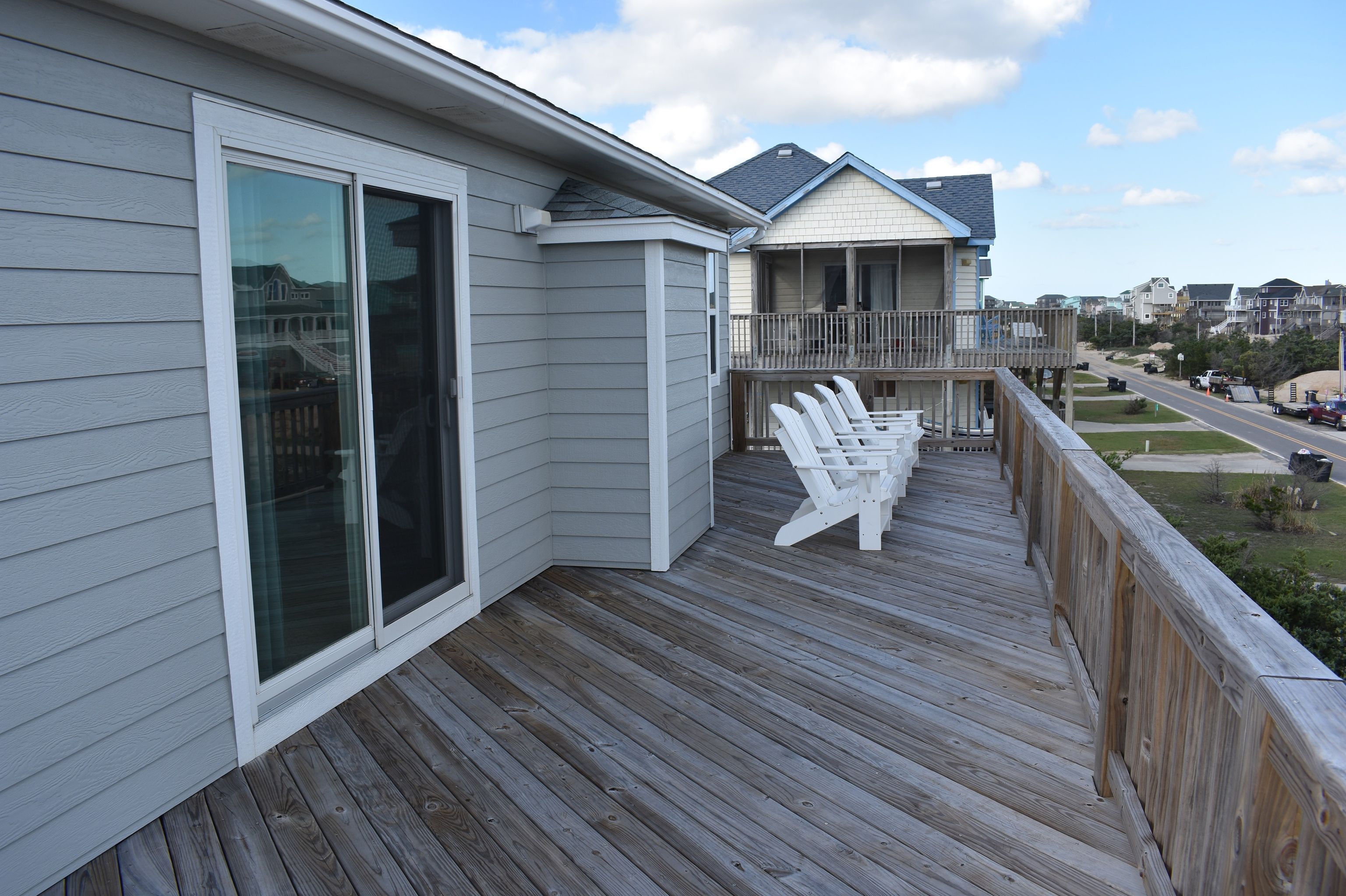 A wooden deck with white chairs and a glass door leading to a balcony.