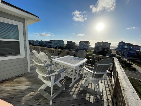 Une terrasse avec une table et des chaises, donnant sur une plage bordée de maisons.