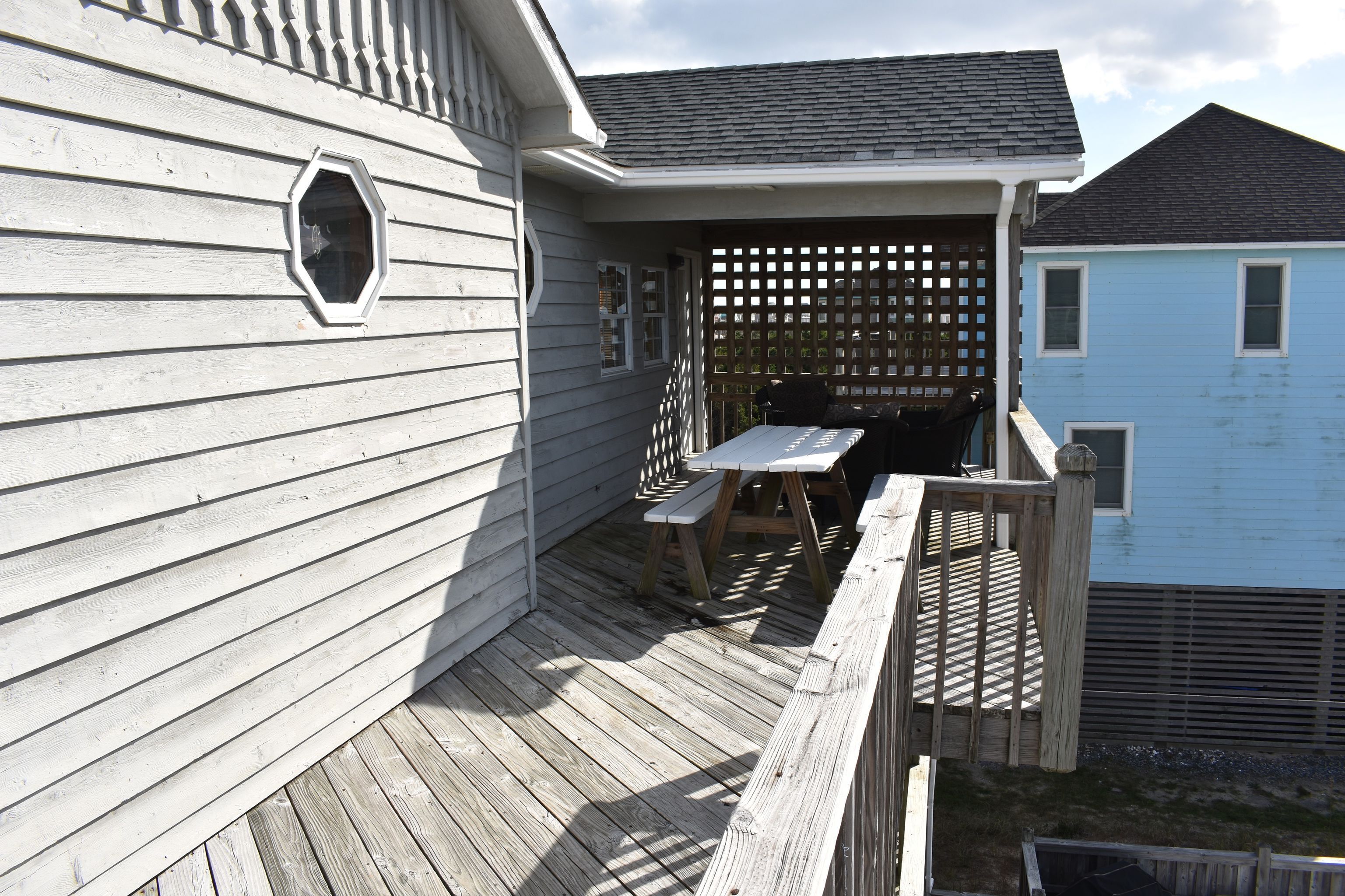 A wooden deck with a picnic table and chairs, a lattice fence, and a small window.
