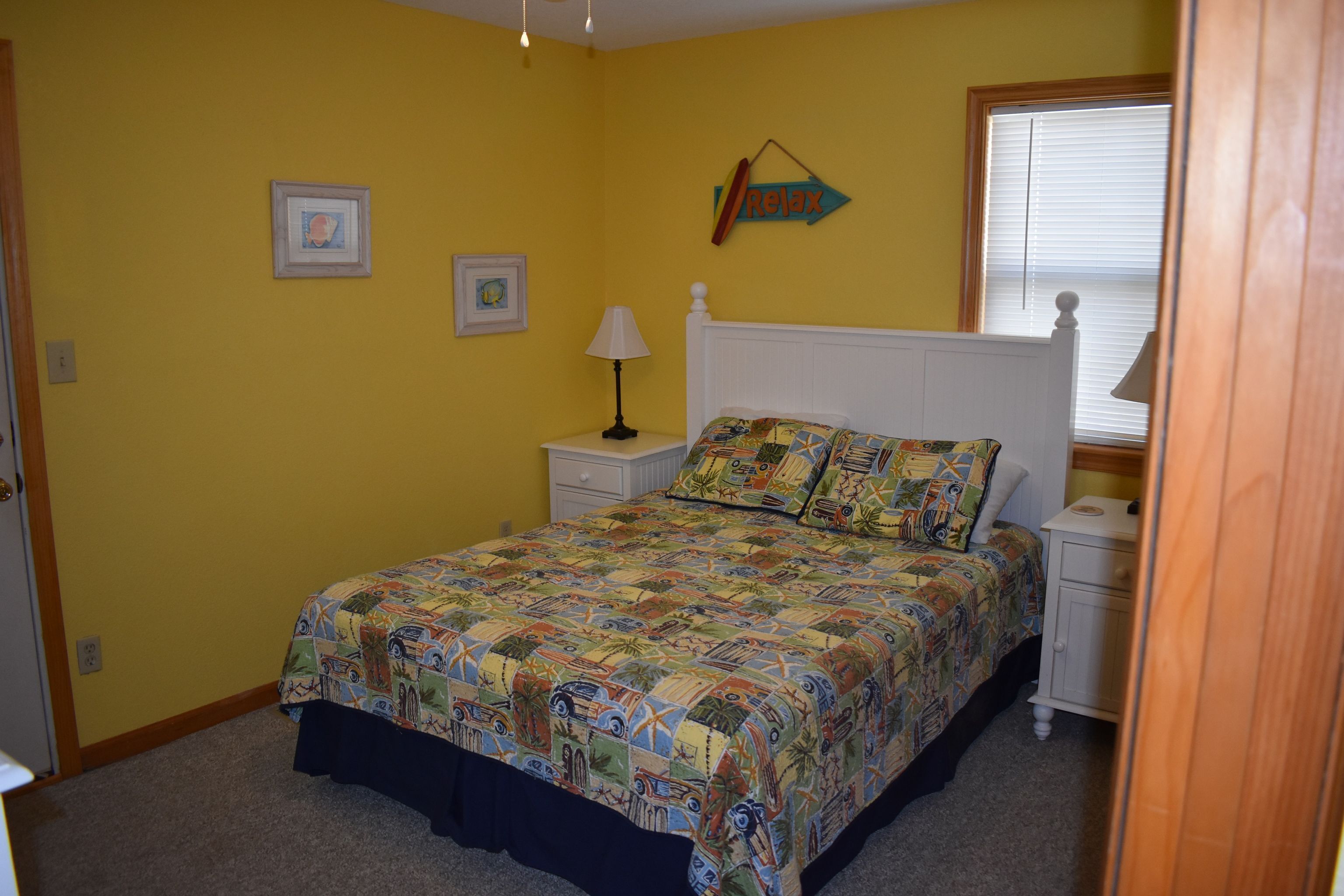 A bedroom with a bed, nightstands, a lamp, and a window with blinds.