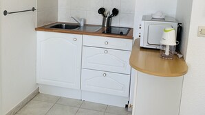 Una cocina compacta con gabinetes blancos, un lavamanos y un microondas.