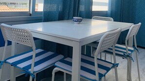 Un comedor con una mesa blanca y cuatro sillas, un bol en la mesa y cortinas azules.