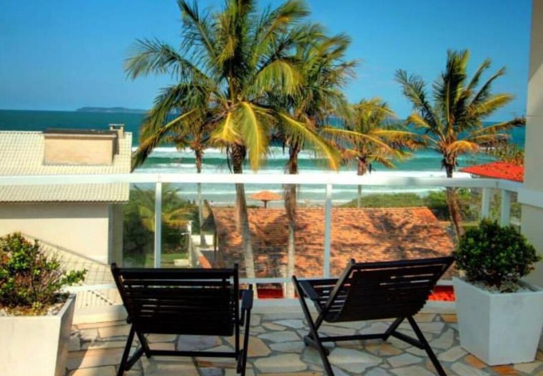 Un balcón con dos sillones de descanso negros, cerramiento de vidrio y vistas a la playa y al océano.
