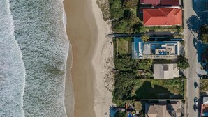 An aerial view of a coastal property with a beach, houses with red roofs, and a tennis court. - Pousada Pedra Salgada (Bombinhas)