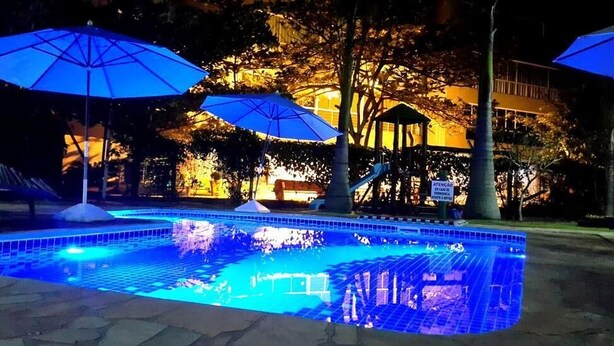A swimming pool with blue lighting, surrounded by trees and umbrellas. - Pousada Pedra Salgada (Bombinhas)