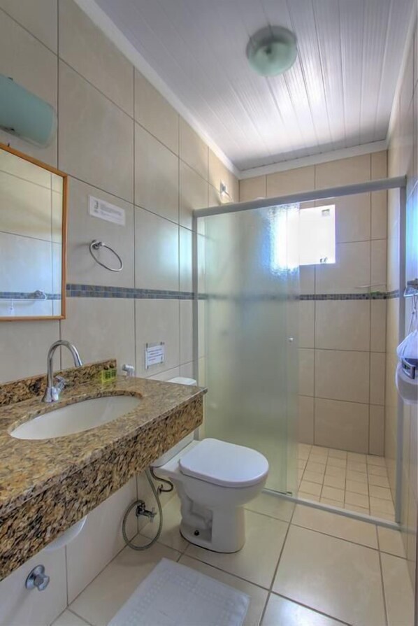 Un baño con lavamanos de encimera de granito, inodoro blanco y ducha con mampara de vidrio.
