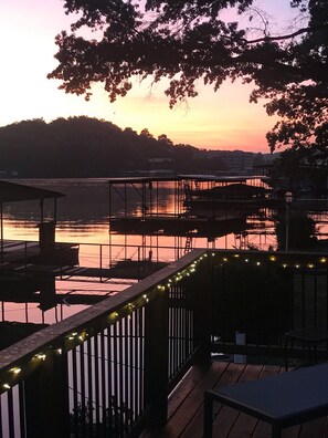A waterfront deck with a railing, a dock, and a view of the water and hills in the background.
