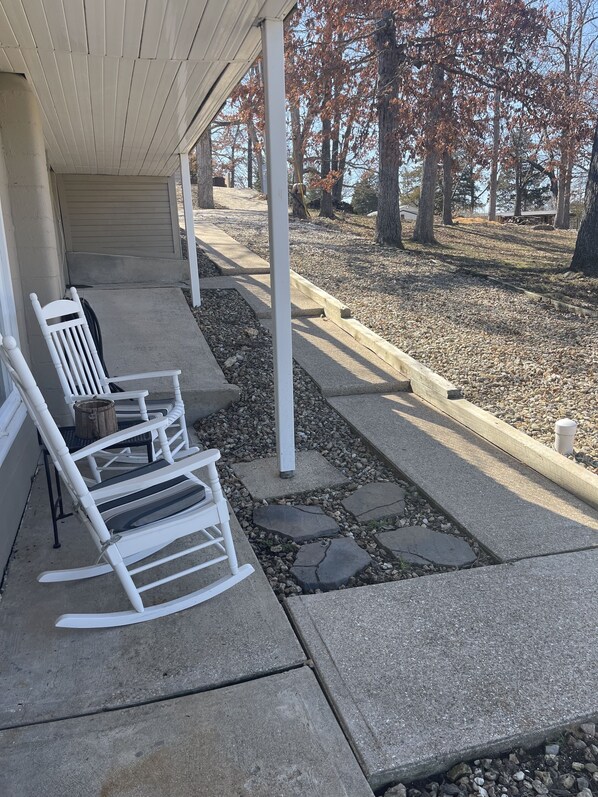A covered porch with white rocking chairs and a concrete pathway.